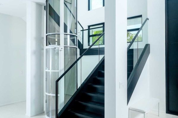 Modern staircase and glass elevator in bright hallway.