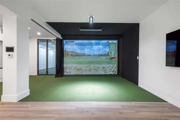 Home golf simulator with green turf and screen