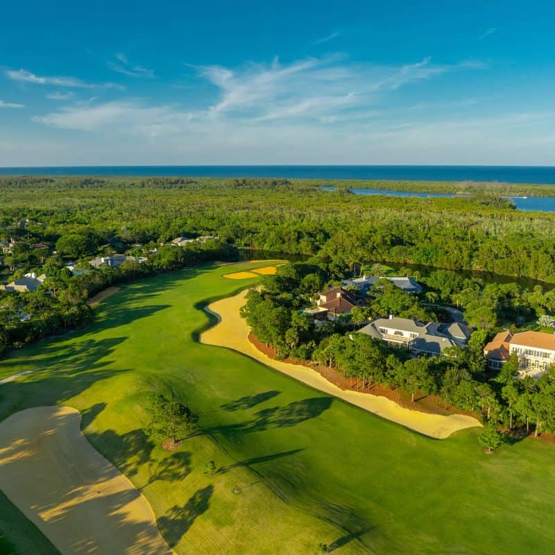 Aerial view of golf course and houses by ocean.