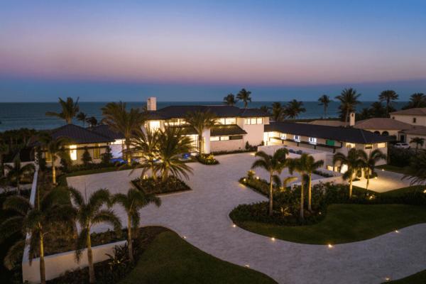 Beachfront mansion at sunset with palm trees.